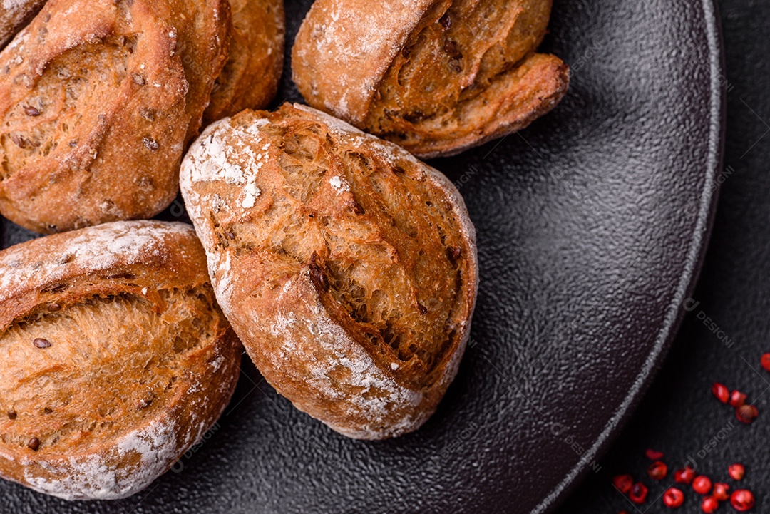 Pãezinhos de pão fresco com sal, especiarias, sementes e grãos sobre fundo escuro