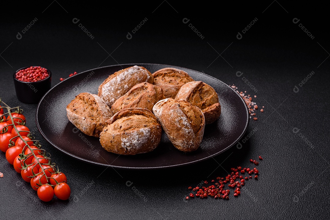 Pãezinhos de pão fresco com sal, especiarias, sementes e grãos sobre fundo escuro