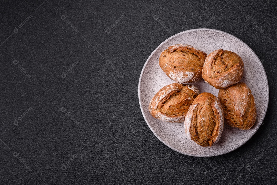 Pãezinhos de pão fresco com sal, especiarias, sementes e grãos sobre fundo escuro