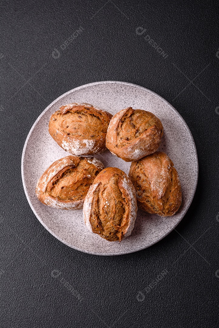 Pãezinhos de pão fresco com sal, especiarias, sementes e grãos sobre fundo escuro