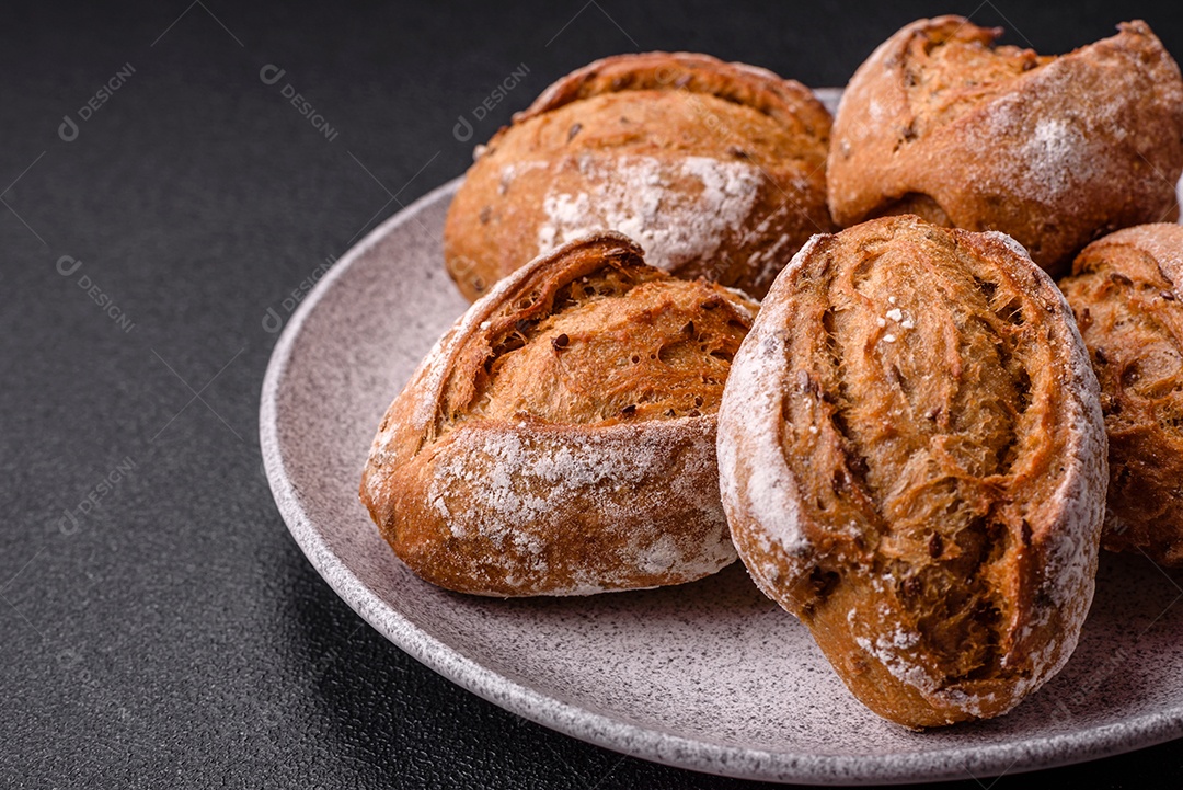 Pãezinhos de pão fresco com sal, especiarias, sementes e grãos sobre fundo escuro
