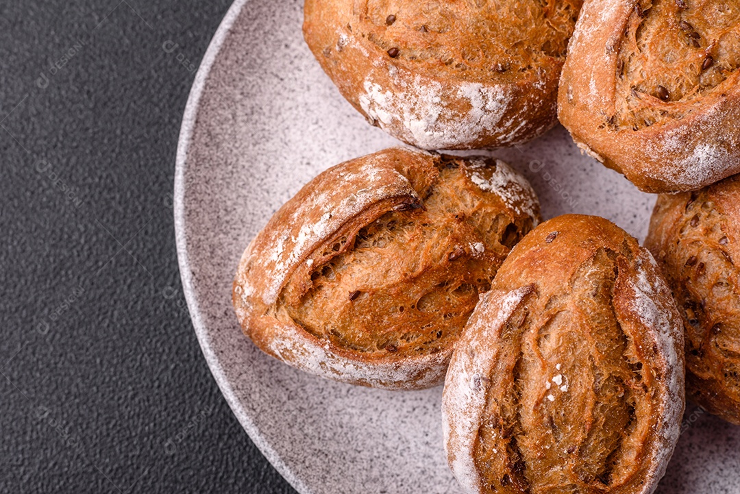 Pãezinhos de pão fresco com sal, especiarias, sementes e grãos sobre fundo escuro