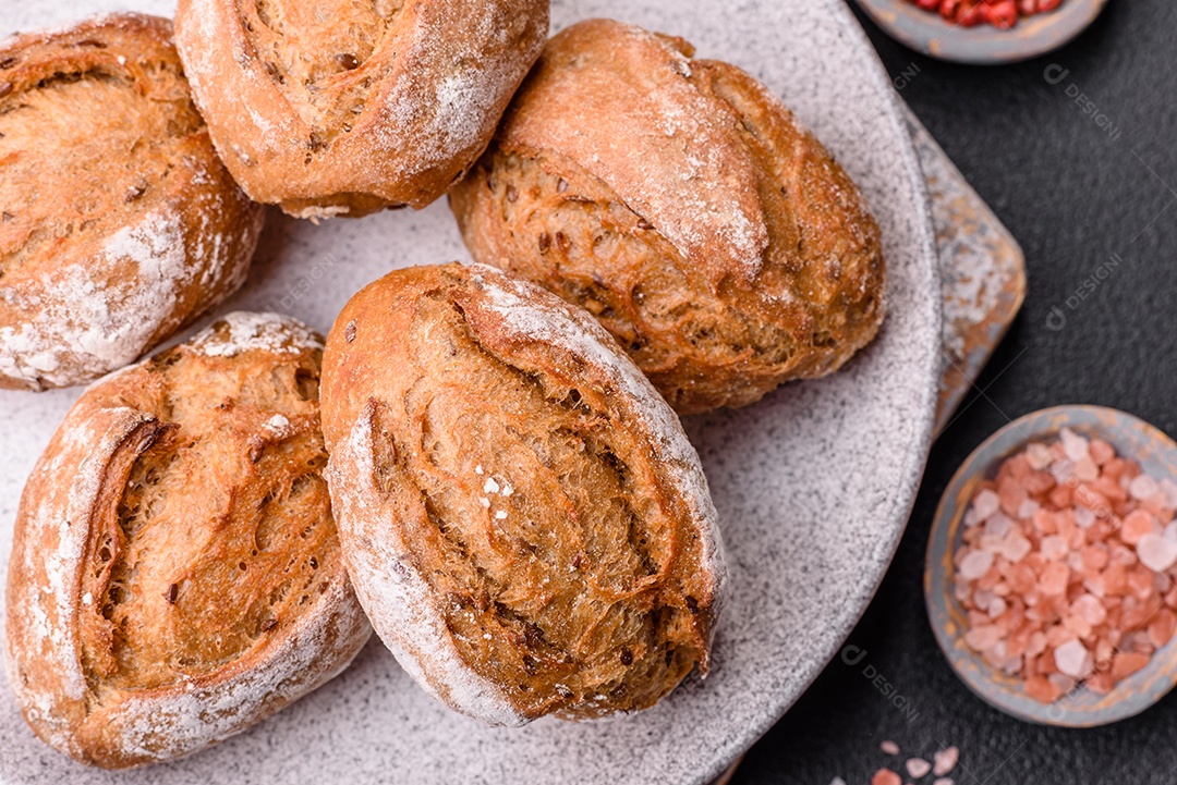 Pãezinhos de pão fresco com sal, especiarias, sementes e grãos sobre fundo escuro