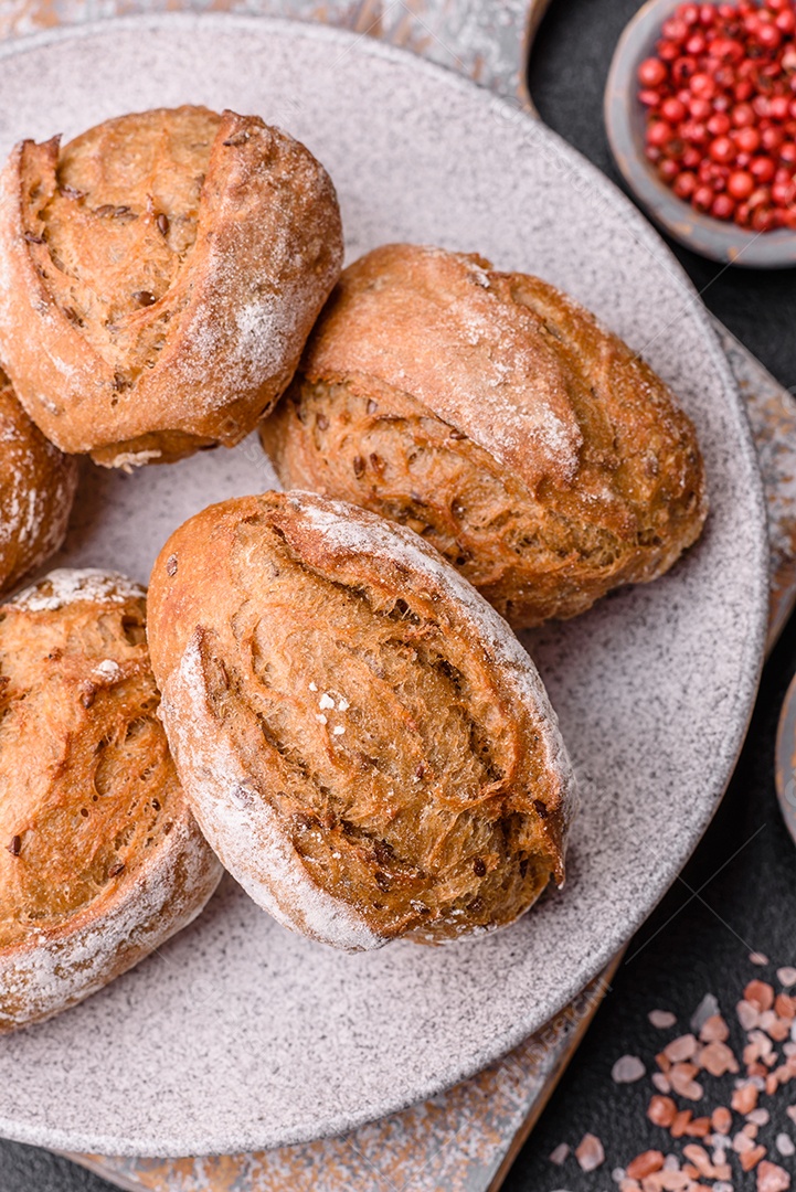 Pãezinhos de pão fresco com sal, especiarias, sementes e grãos sobre fundo escuro