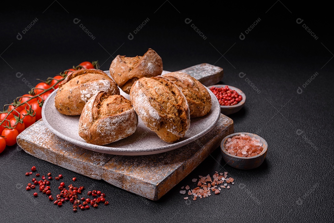 Pãezinhos de pão fresco com sal, especiarias, sementes e grãos sobre fundo escuro