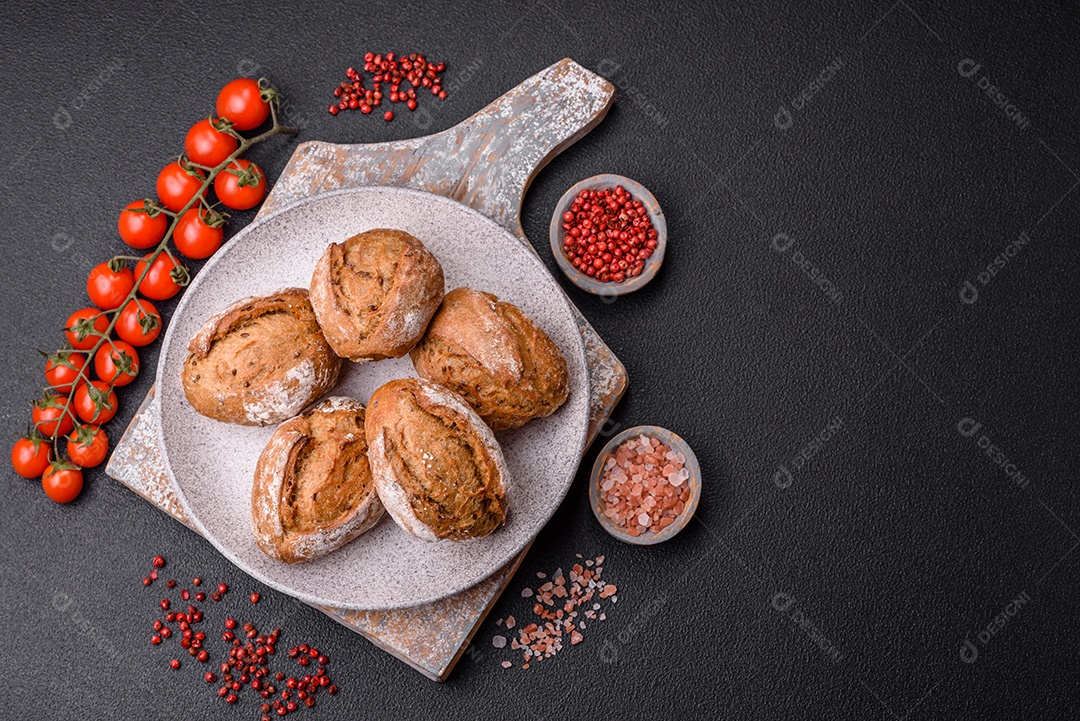 Pãezinhos de pão fresco com sal, especiarias, sementes e grãos sobre fundo escuro