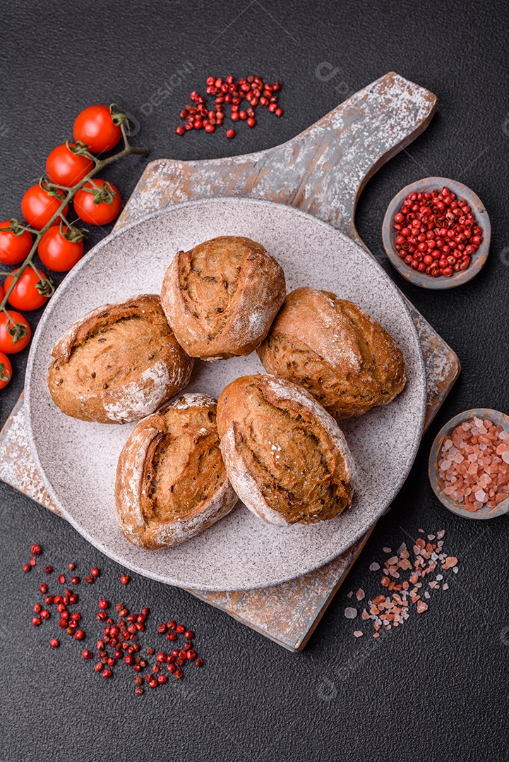 Pãezinhos de pão fresco com sal, especiarias, sementes e grãos sobre fundo escuro