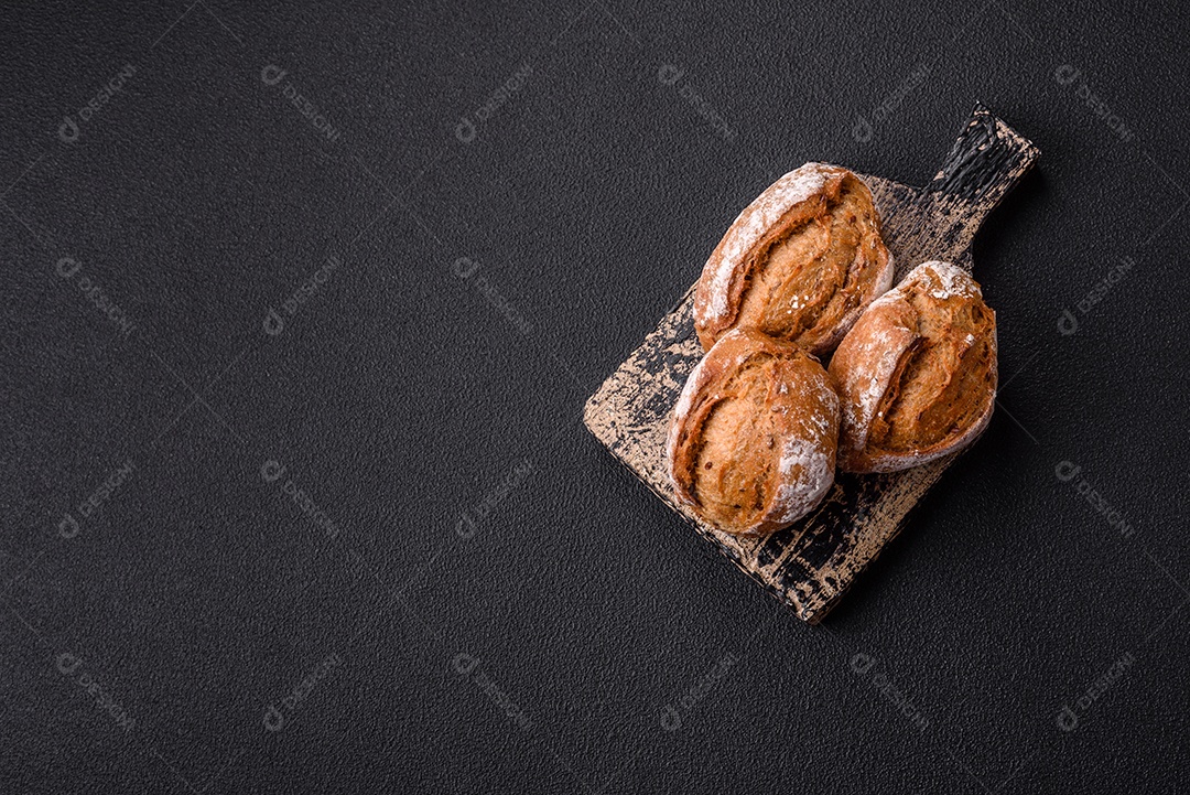 Pãezinhos de pão fresco com sal, especiarias, sementes e grãos sobre fundo escuro