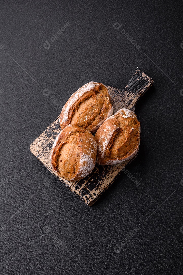 Pãezinhos de pão fresco com sal, especiarias, sementes e grãos sobre fundo escuro