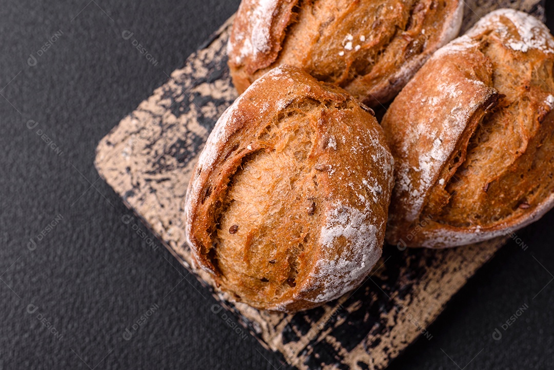 Pãezinhos de pão fresco com sal, especiarias, sementes e grãos sobre fundo escuro