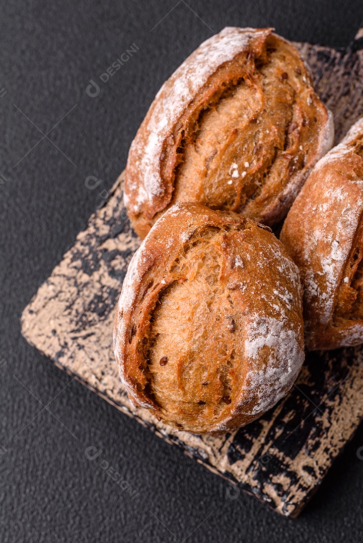 Pãezinhos de pão fresco com sal, especiarias, sementes e grãos sobre fundo escuro