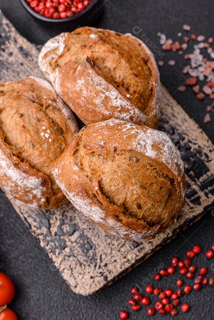 Pãezinhos de pão fresco com sal, especiarias, sementes e grãos sobre fundo escuro