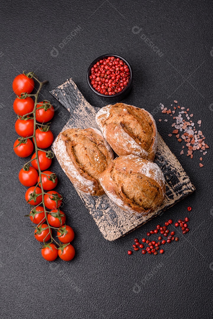 Pãezinhos de pão fresco com sal, especiarias, sementes e grãos sobre fundo escuro
