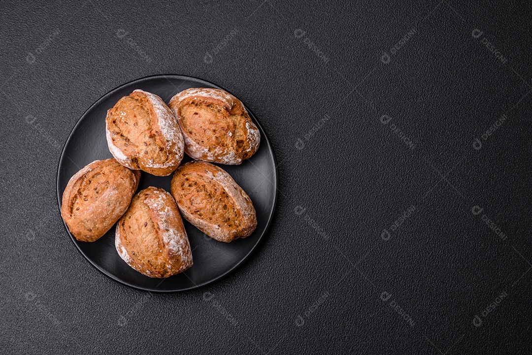 Pãezinhos de pão fresco com sal, especiarias, sementes e grãos sobre fundo escuro