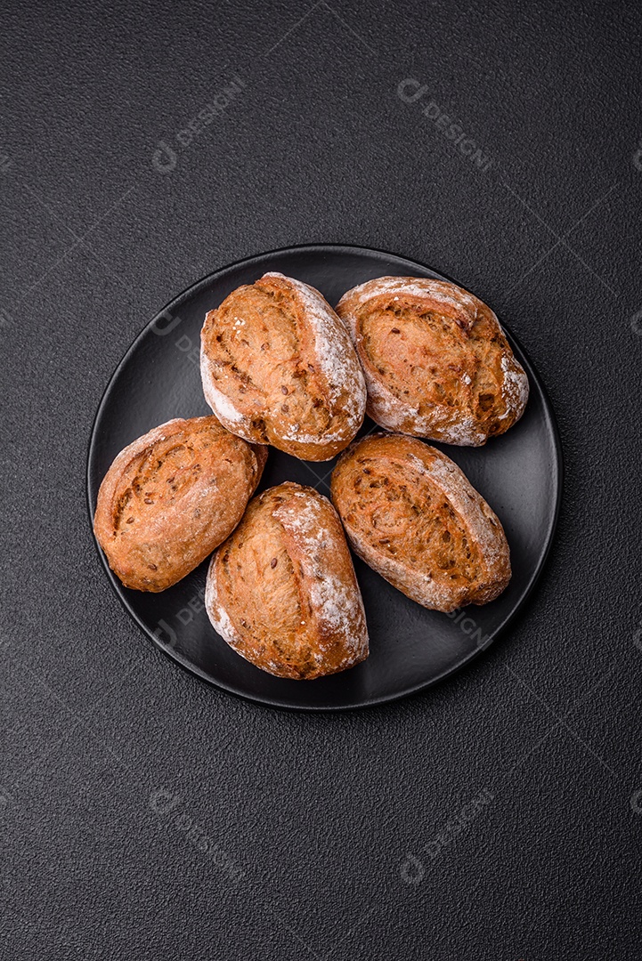 Pãezinhos de pão fresco com sal, especiarias, sementes e grãos sobre fundo escuro