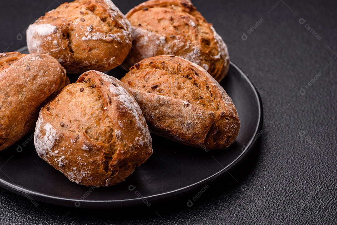 Pãezinhos de pão fresco com sal, especiarias, sementes e grãos sobre fundo escuro