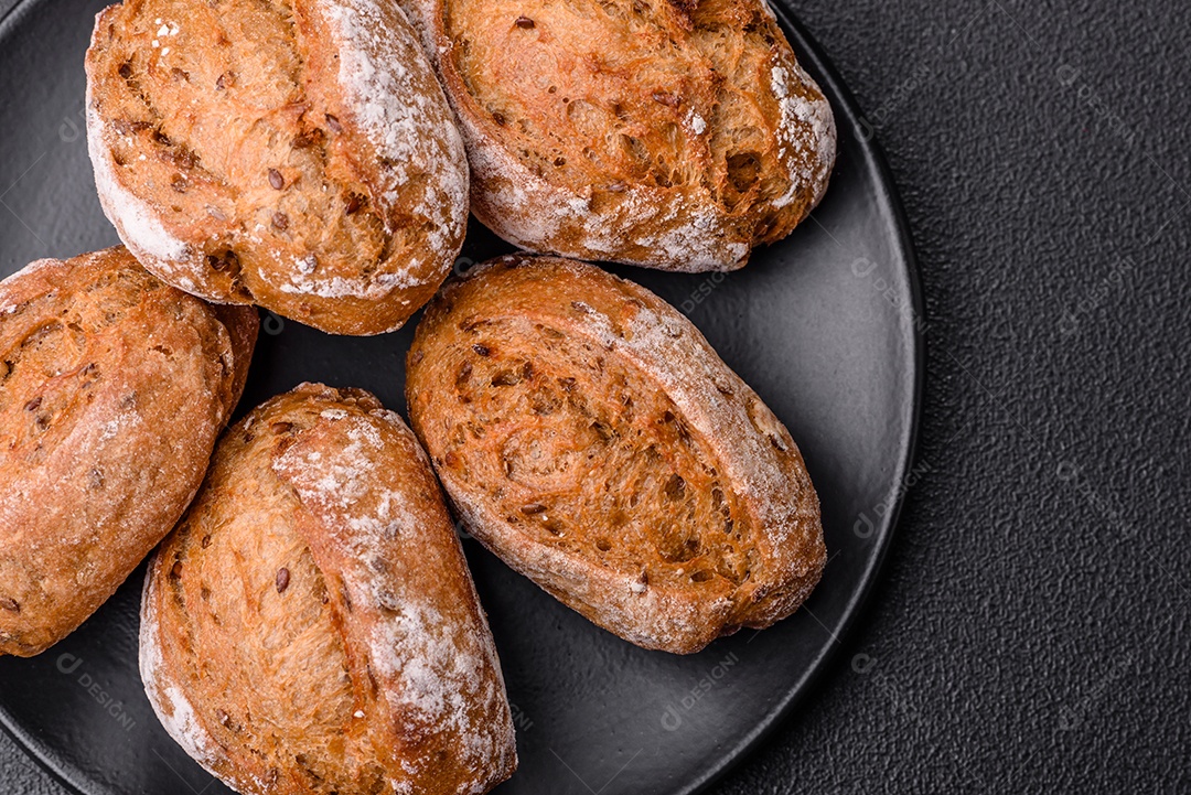 Pãezinhos de pão fresco com sal, especiarias, sementes e grãos sobre fundo escuro