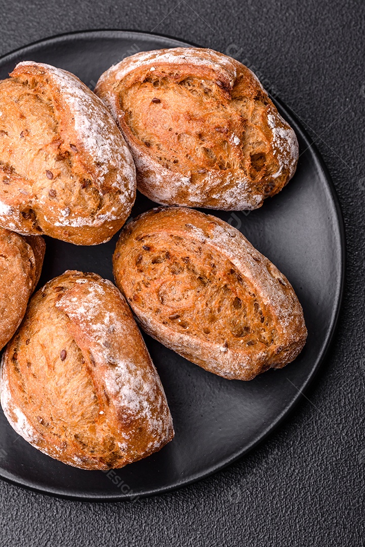 Pãezinhos de pão fresco com sal, especiarias, sementes e grãos sobre fundo escuro