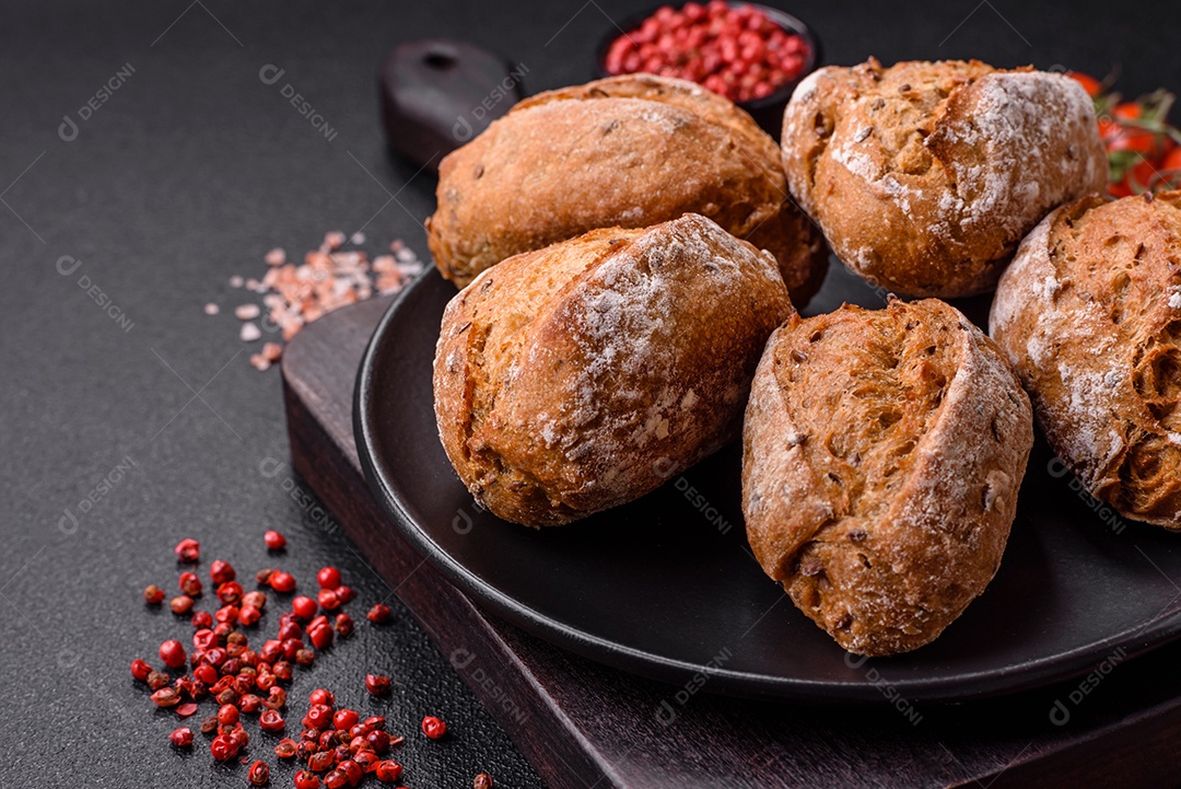 Pãezinhos de pão fresco com sal, especiarias, sementes e grãos sobre fundo escuro