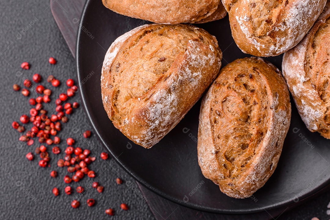 Pãezinhos de pão fresco com sal, especiarias, sementes e grãos sobre fundo escuro