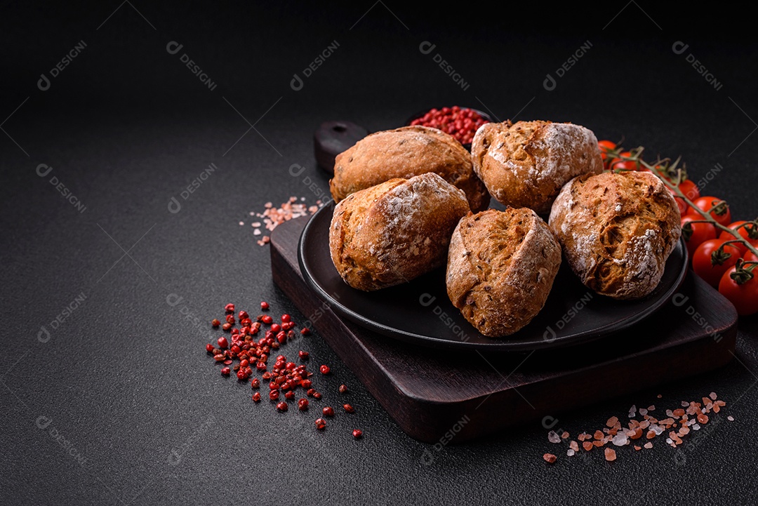 Pãezinhos de pão fresco com sal, especiarias, sementes e grãos sobre fundo escur