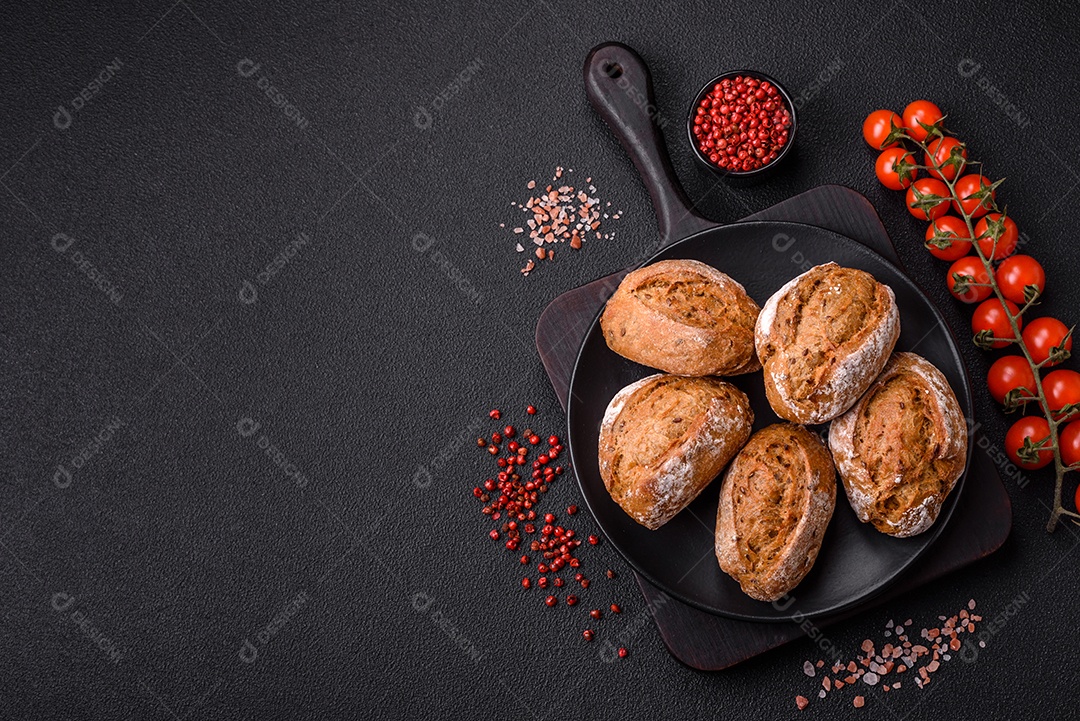 Pãezinhos de pão fresco com sal, especiarias, sementes e grãos sobre fundo escuro