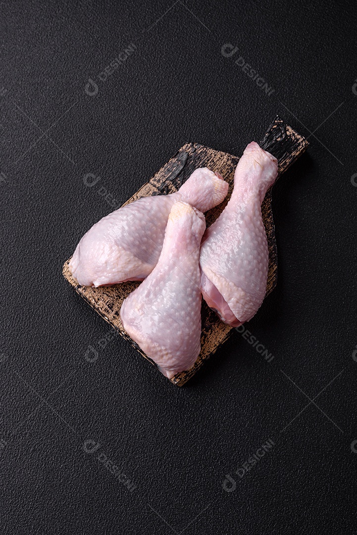 Coxas de frango cru fresco com sal e especiarias em fundo escuro de concreto