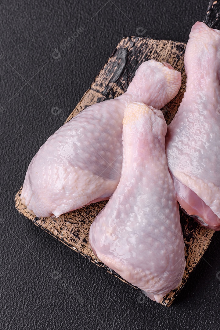 Coxas de frango cru fresco com sal e especiarias em fundo escuro de concreto