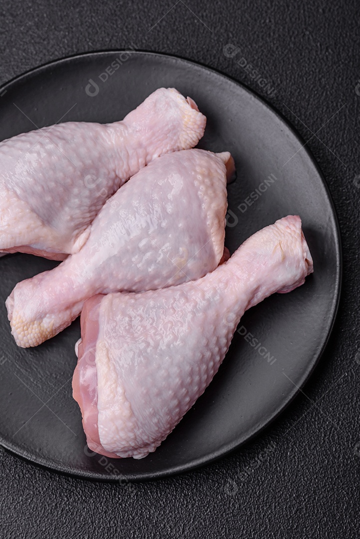 Coxas de frango cru fresco com sal e especiarias em fundo escuro de concreto