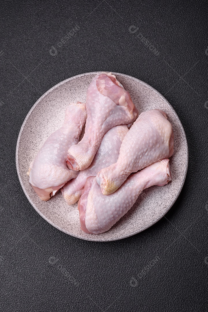 Coxas de frango cru fresco com sal e especiarias em fundo escuro de concreto