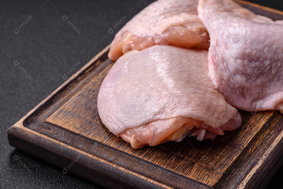 Coxas de frango cru fresco com sal e especiarias em fundo escuro de concreto