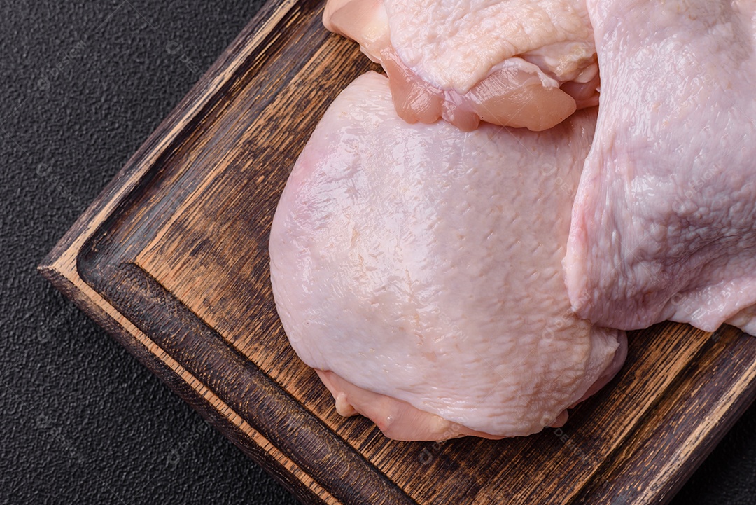 Coxas de frango cru fresco com sal e especiarias em fundo escuro de concreto