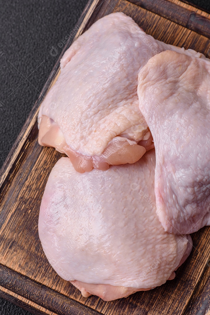 Coxas de frango cru fresco com sal e especiarias em fundo escuro de concreto