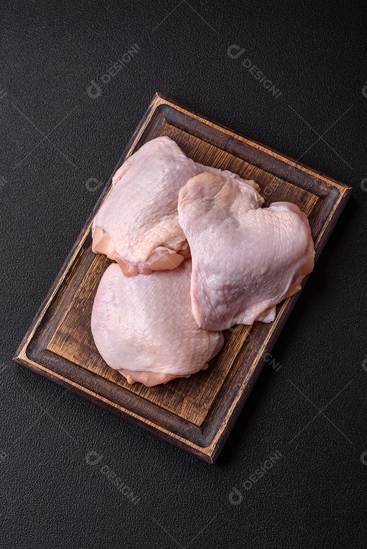 Coxas de frango cru fresco com sal e especiarias em fundo escuro de concreto