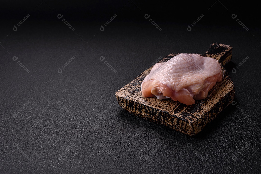 Coxas de frango cru fresco com sal e especiarias em fundo escuro de concreto