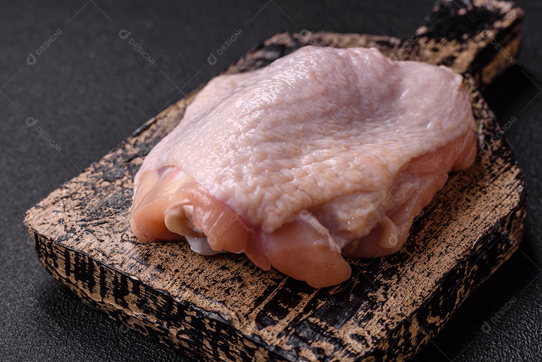 Coxas de frango cru fresco com sal e especiarias em fundo escuro de concreto