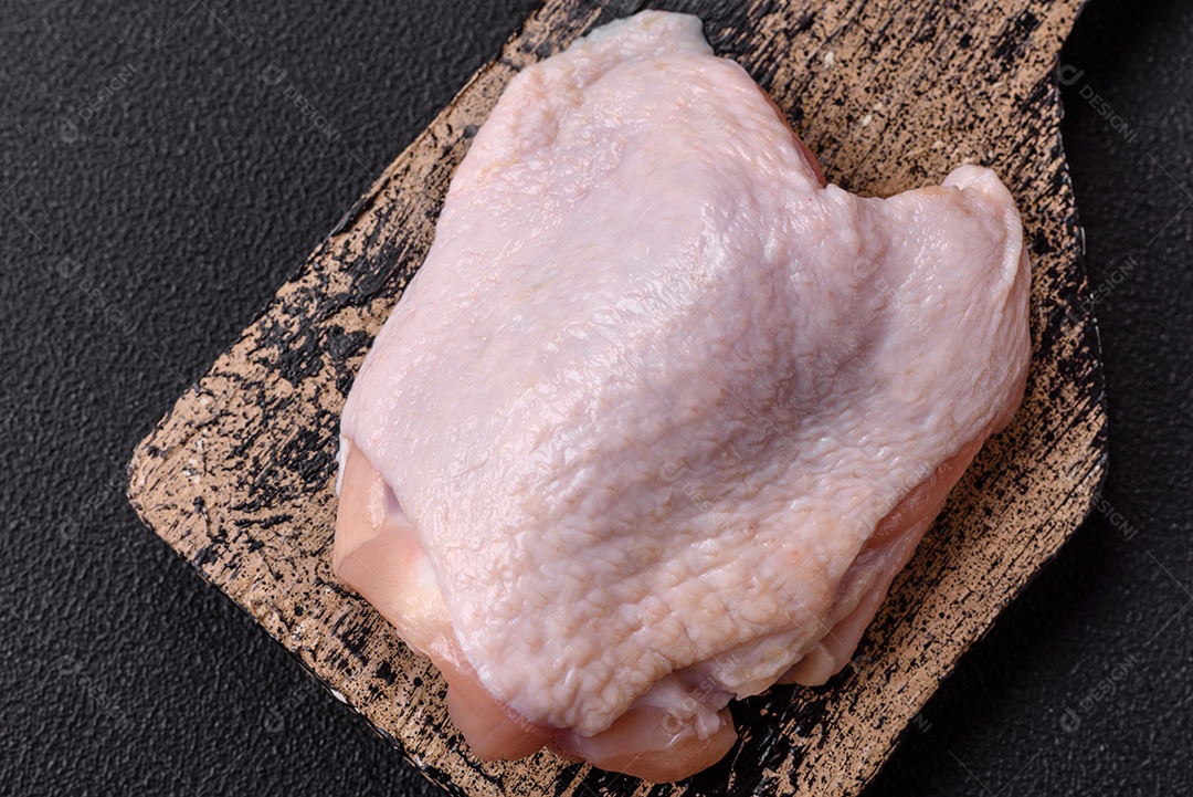 Coxas de frango cru fresco com sal e especiarias em fundo escuro de concreto