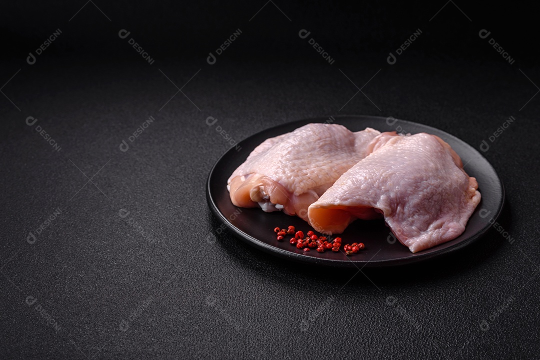 Coxas de frango cru fresco com sal e especiarias em fundo escuro de concreto