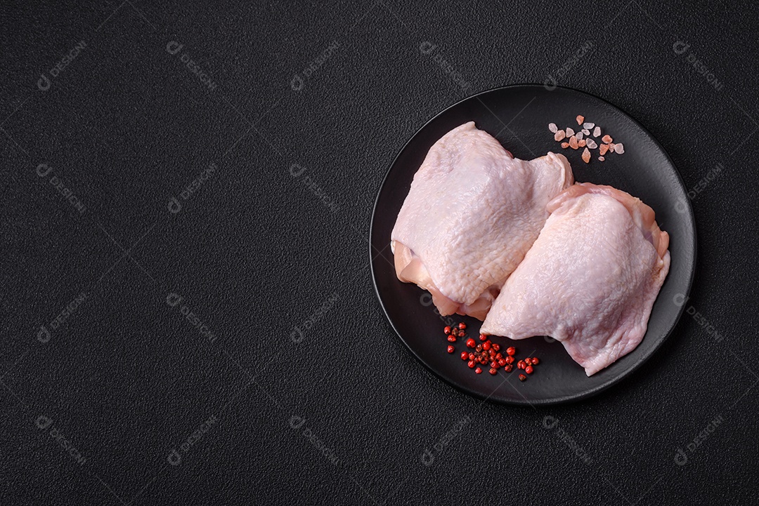 Coxas de frango cru fresco com sal e especiarias em fundo escuro de concreto