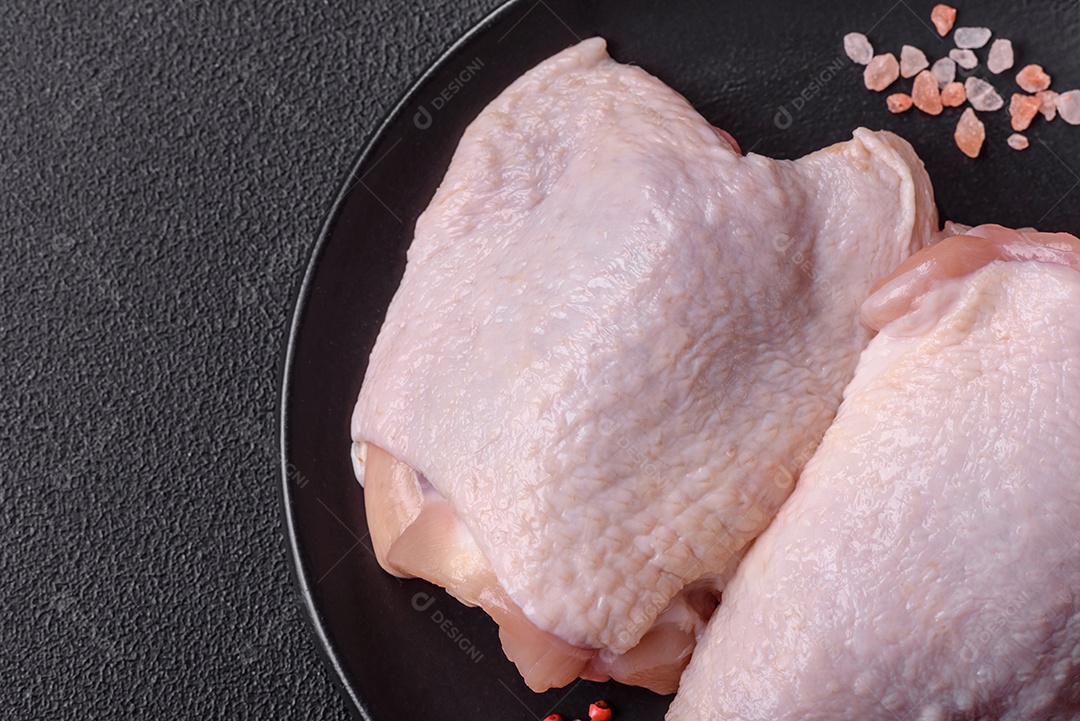 Coxas de frango cru fresco com sal e especiarias em fundo escuro de concreto