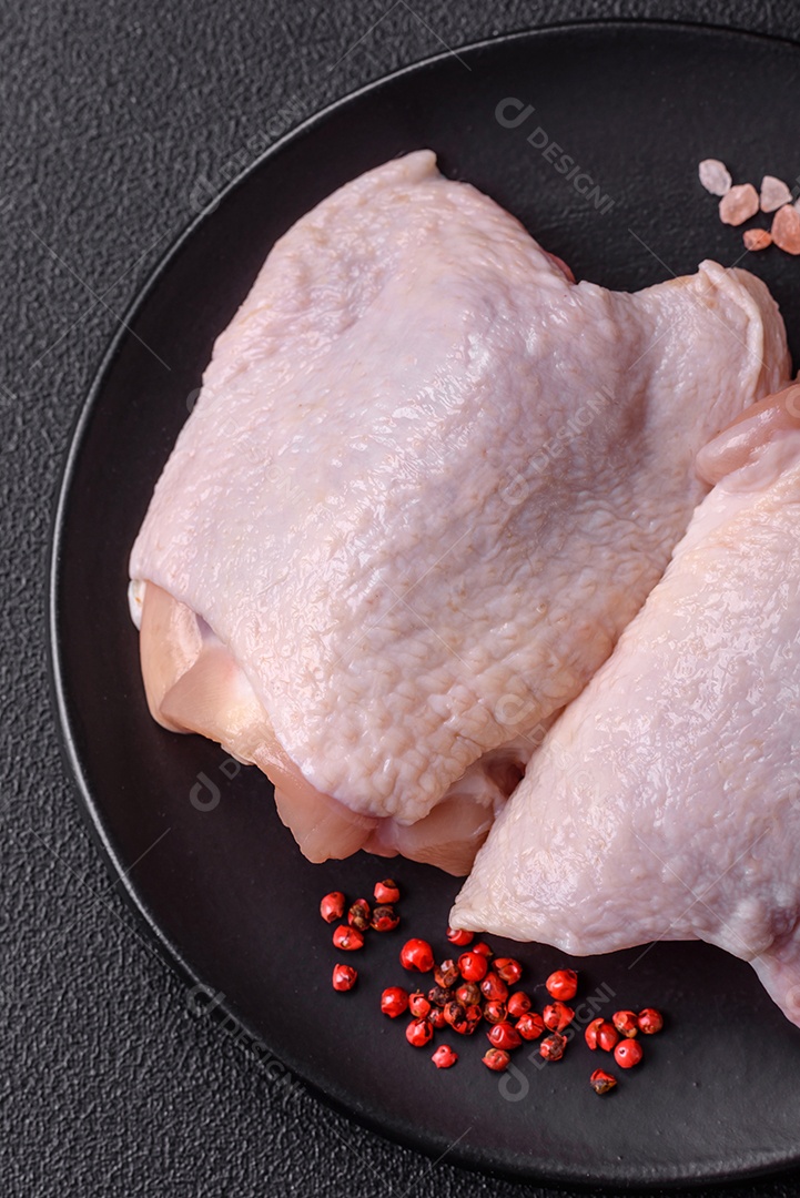 Coxas de frango cru fresco com sal e especiarias em fundo escuro de concreto