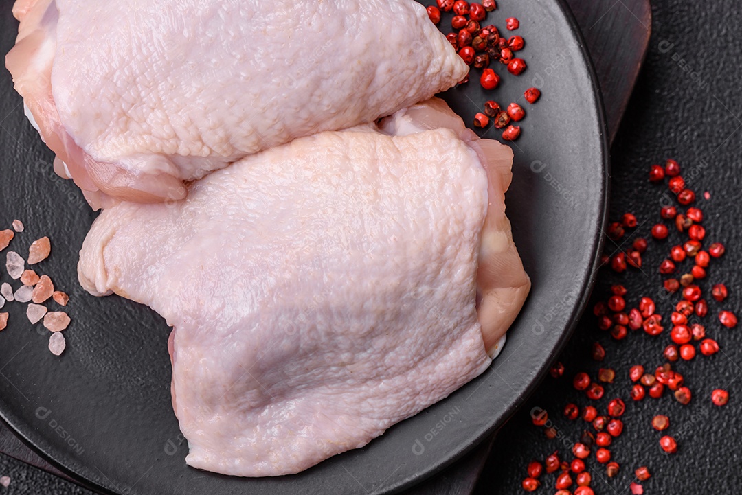 Coxas de frango cru fresco com sal e especiarias em fundo escuro de concreto