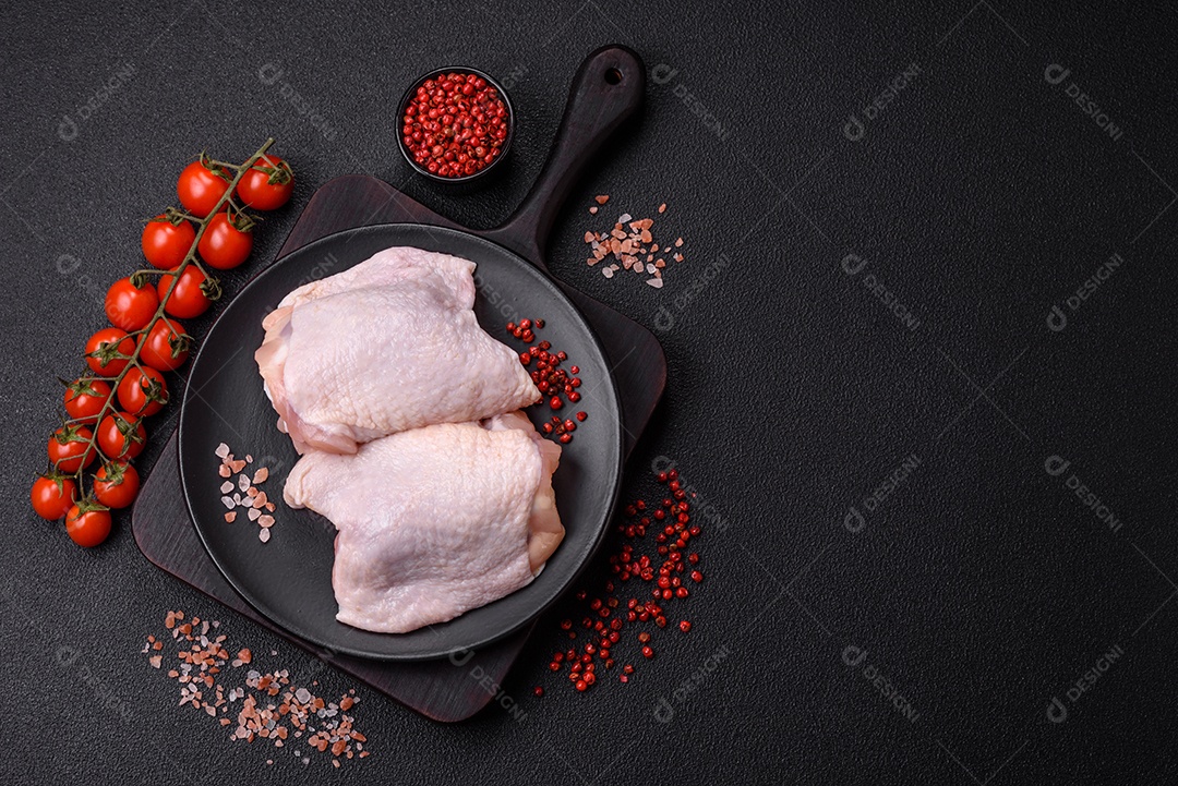 Coxas de frango cru fresco com sal e especiarias em fundo escuro de concreto