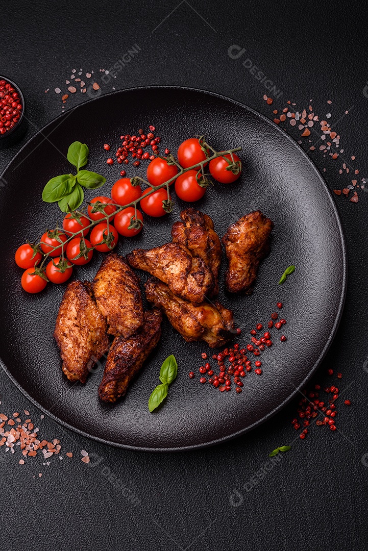 Deliciosas asas de frango suculentas assadas na grelha com sal, especiarias e ervas sobre um fundo escuro de concreto