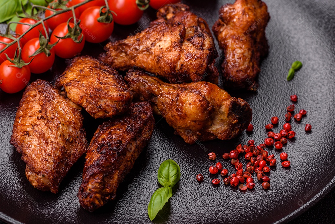 Deliciosas asas de frango suculentas assadas na grelha com sal, especiarias e ervas sobre um fundo escuro de concreto