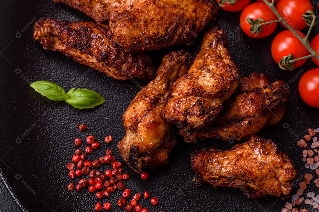 Deliciosas asas de frango suculentas assadas na grelha com sal, especiarias e ervas sobre um fundo escuro de concreto