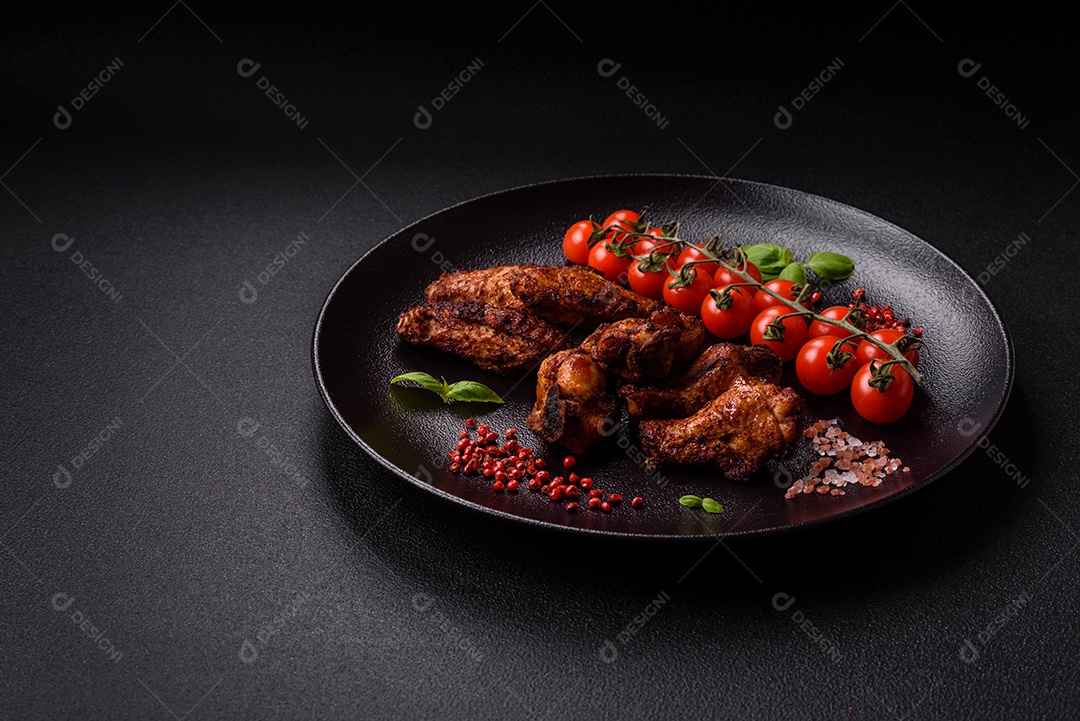 Deliciosas asas de frango suculentas assadas na grelha com sal, especiarias e ervas sobre um fundo escuro de concreto