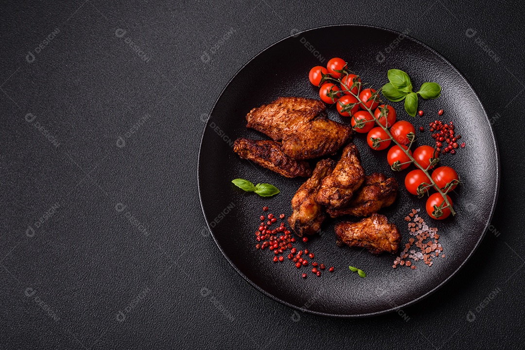 Deliciosas asas de frango suculentas assadas na grelha com sal, especiarias e ervas sobre um fundo escuro de concreto