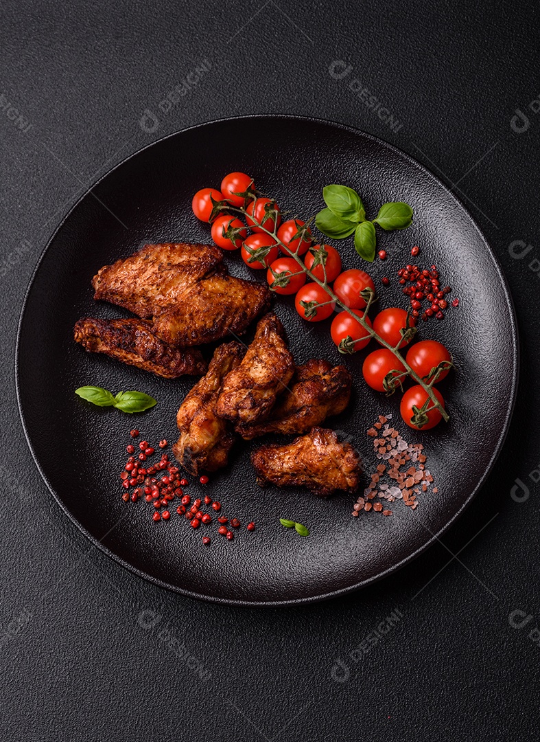 Deliciosas asas de frango suculentas assadas na grelha com sal, especiarias e ervas sobre um fundo escuro de concreto