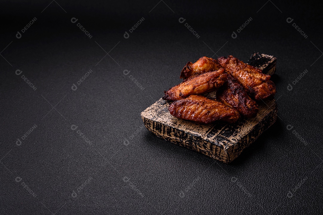 Deliciosas asas de frango suculentas assadas na grelha com sal, especiarias e ervas sobre um fundo escuro de concreto